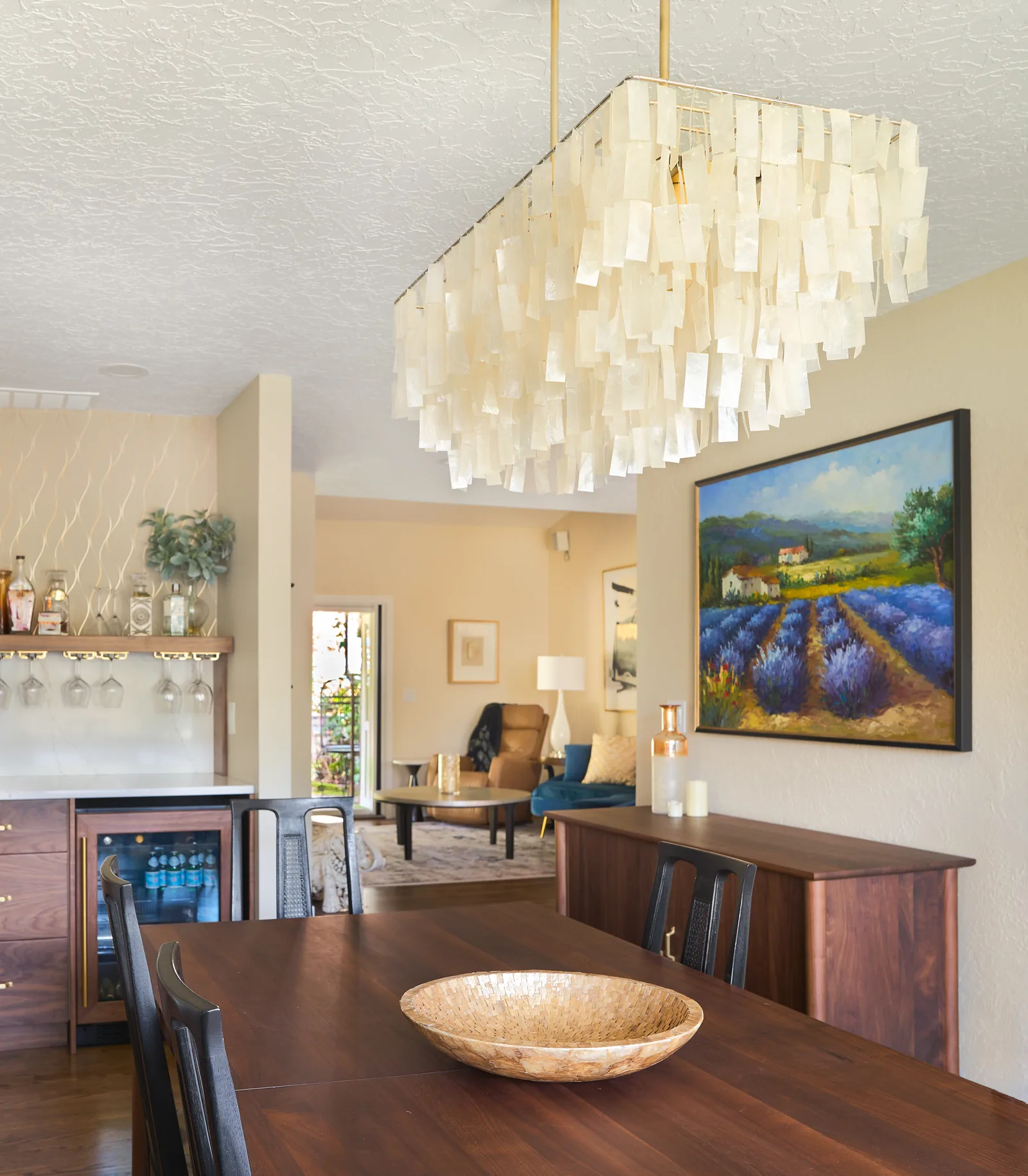 Dining room under a capiz shell chandelier, with the walnut bar beyond
